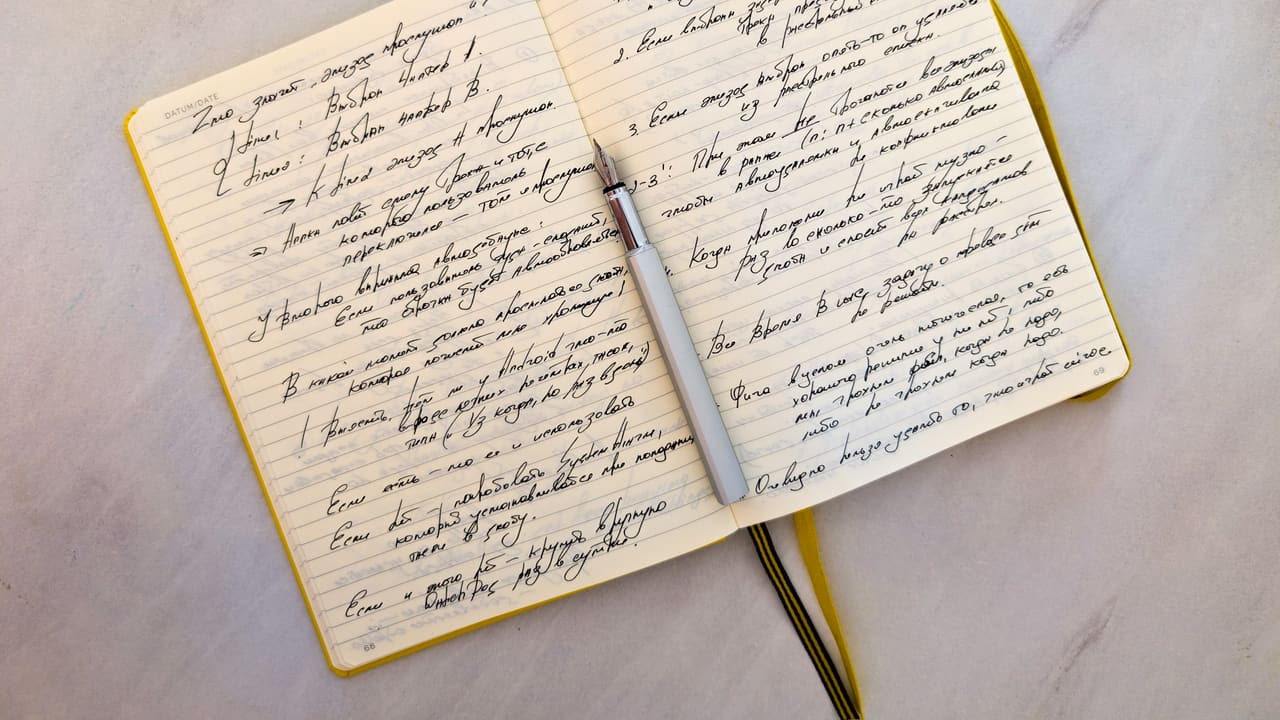 Open notebook with cursive handwritten notes on a marble surface, a pen resting on the pages.