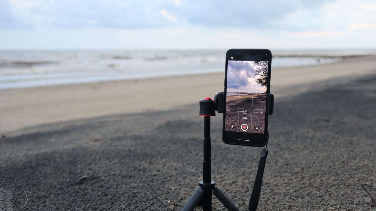 A smartphone on a tripod recording a beach scene.
