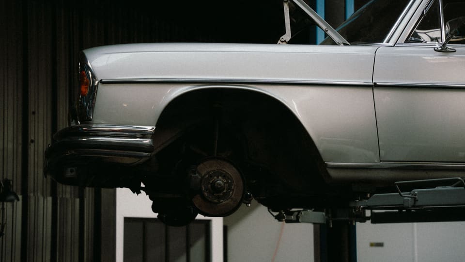 A classic car is elevated on a lift in a professional auto repair garage, showcasing its undercarriage.