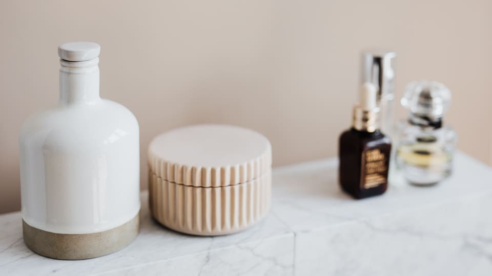 Set of reusable cosmetic containers for cream and shampoo arranged near various skincare products and perfume bottle on white marble shelf against beige wall in modern bathroom interior