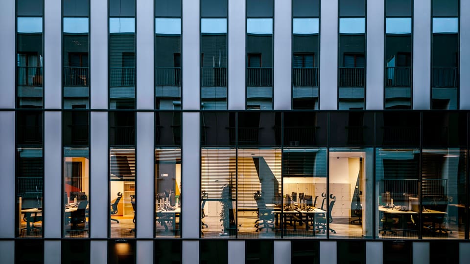 Illuminated office inside a modern glass building exterior, showcasing architecture and workspace design.