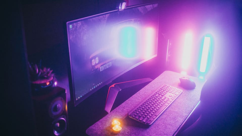 A stylish gaming desk featuring neon lights, keyboard, and monitor in a dark room.