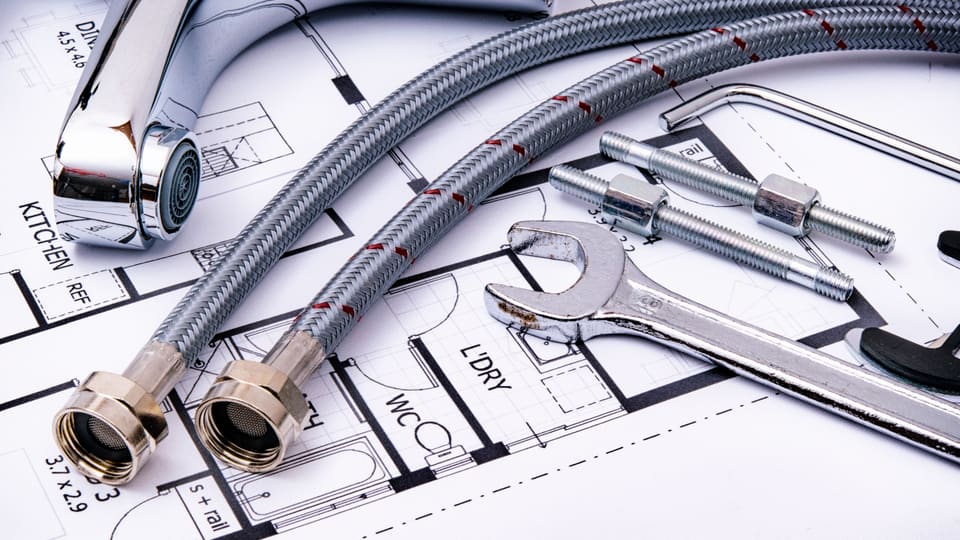 Close-up of plumbing tools and faucet on top of an architectural blueprint, perfect for hardware and construction themes.