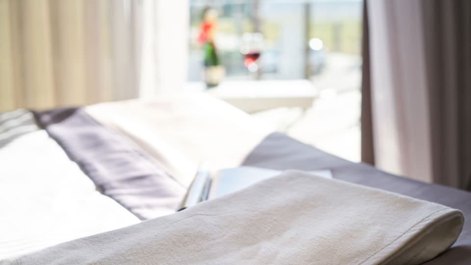 A well-lit modern hotel room with fresh towels and wine, offering a relaxing atmosphere.