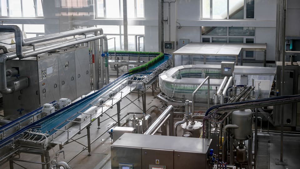 Interior view of an automated beverage bottling factory with machinery and conveyor belts.