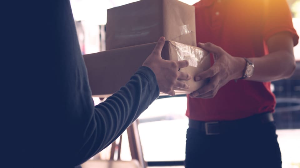 Close-up of a delivery service worker handing over packages to a customer indoors.