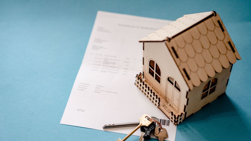 Miniature wooden house with keys and contract symbolizing real estate transactions.