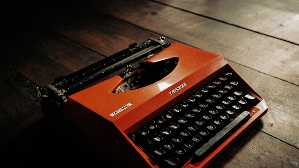 Close-up of a vintage orange typewriter placed on a rustic wooden floor, exuding a nostalgic feel.