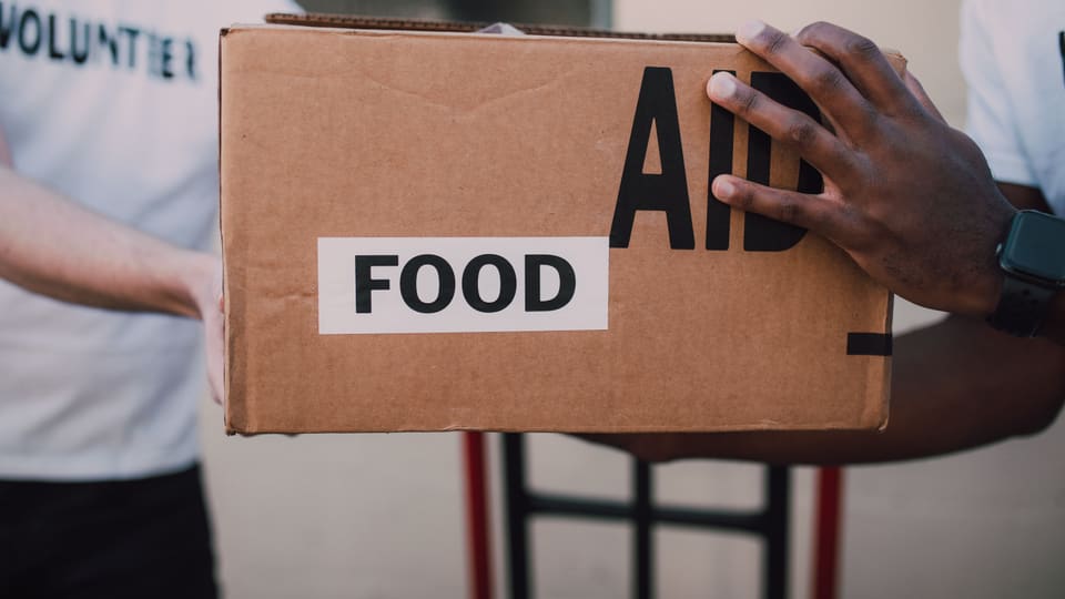 Two volunteers handing over a box labeled 'Food Aid', symbolizing community support.