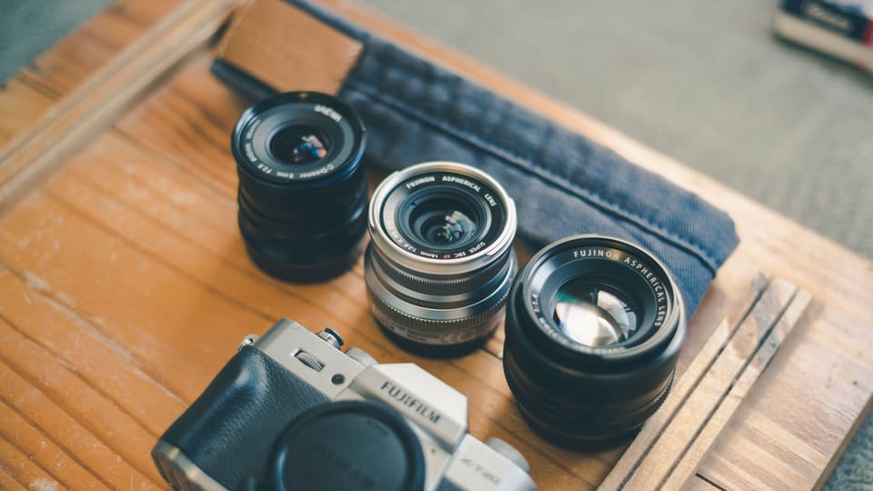 A close-up shot displaying camera gear including a Fujifilm body and lenses on a wooden table.