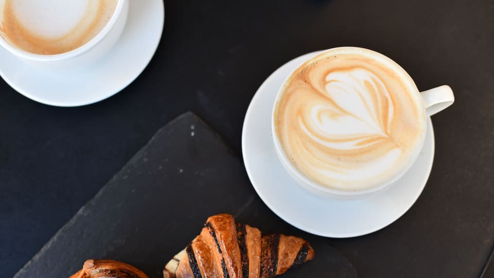 Top view of frothy cappuccino and croissants on a slate plate, perfect breakfast setup.