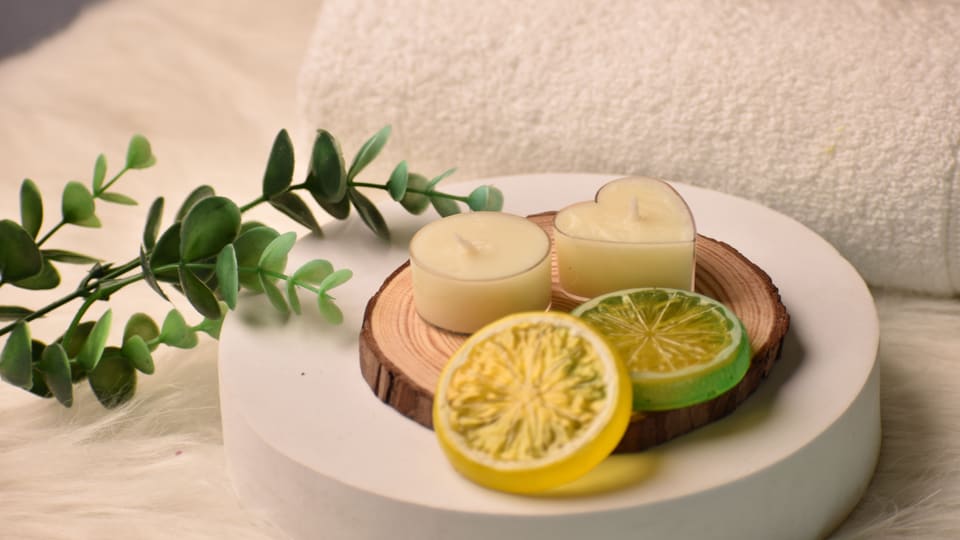 Relaxing spa scene with candles, citrus slices, towel, and eucalyptus on soft background.