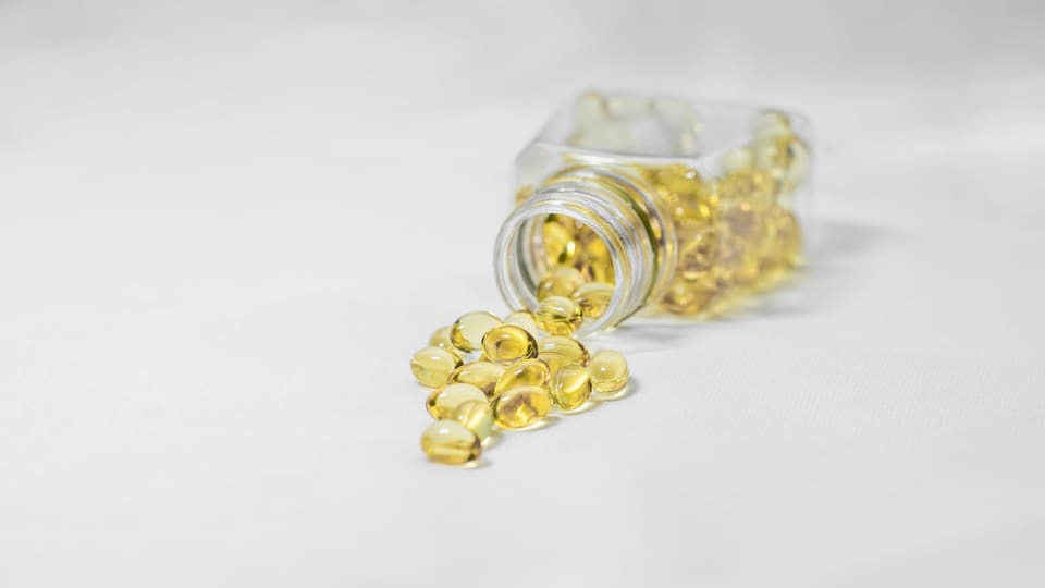 Close-up of yellow softgel capsules spilled from a glass bottle on a white surface.